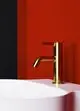 Standventil in gebürstetem Gold, montiert über einem weißen Waschbecken, vor rot-schwarzer Wand. Produkt von Ideal Standard.